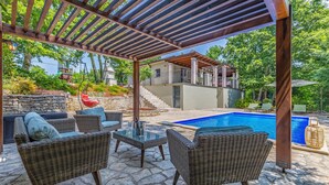 A covered outdoor seating area with wicker furniture, a pool, and a stone patio.