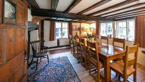 A traditional dining room with wooden furniture, a patterned rug, and large windows with curtains. - Just So Cottage (Buckingham)
