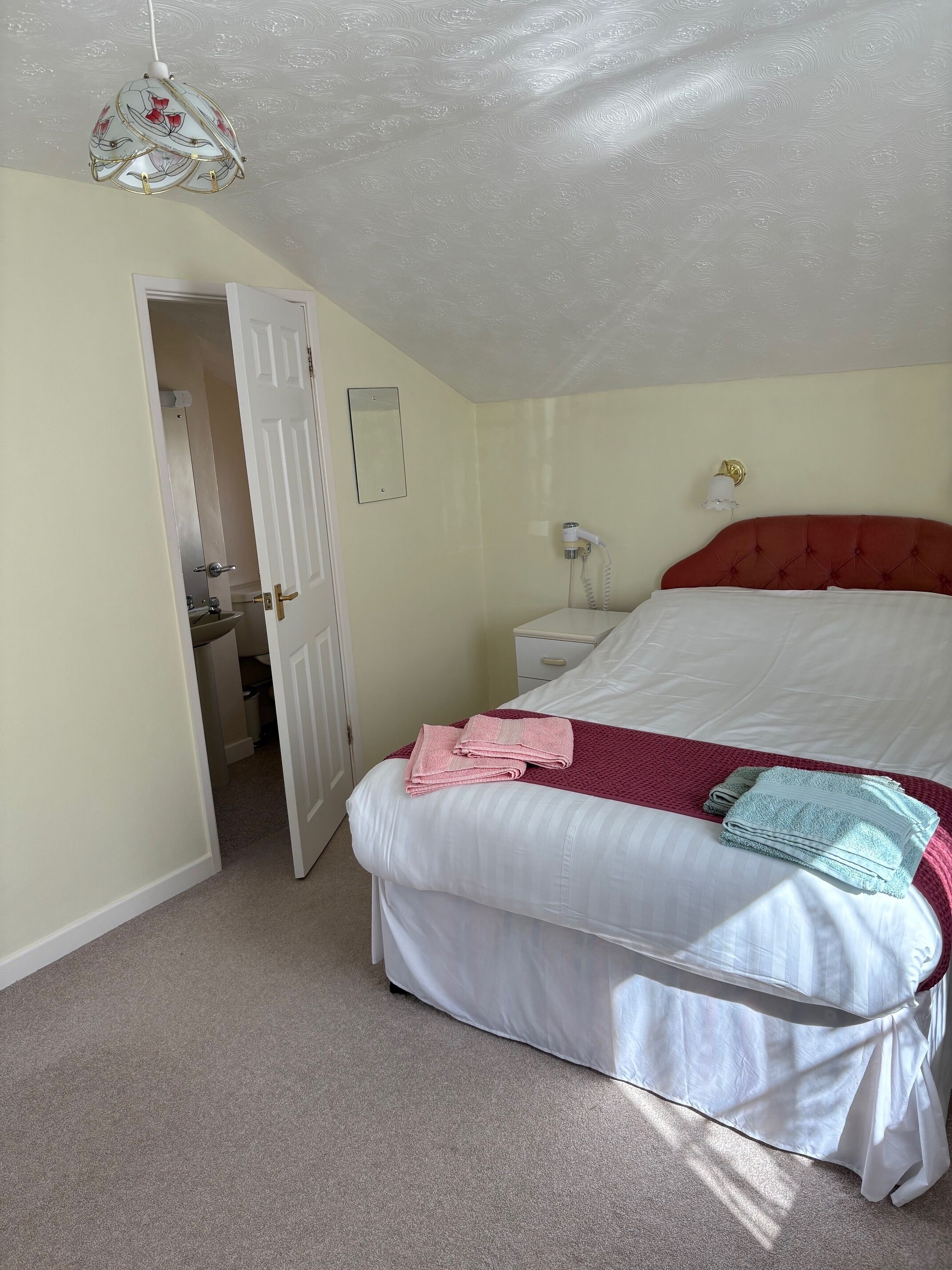 A bedroom with a bed, bedside table, and a hanging light fixture.