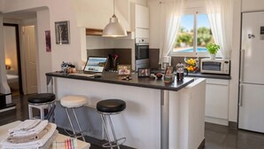 Eine moderne Küche mit einer zentralen Kochinsel, Barhocker, einem Esstisch mit Handtüchern, einem Laptop, einer Mikrowelle und Blick ins Freie.