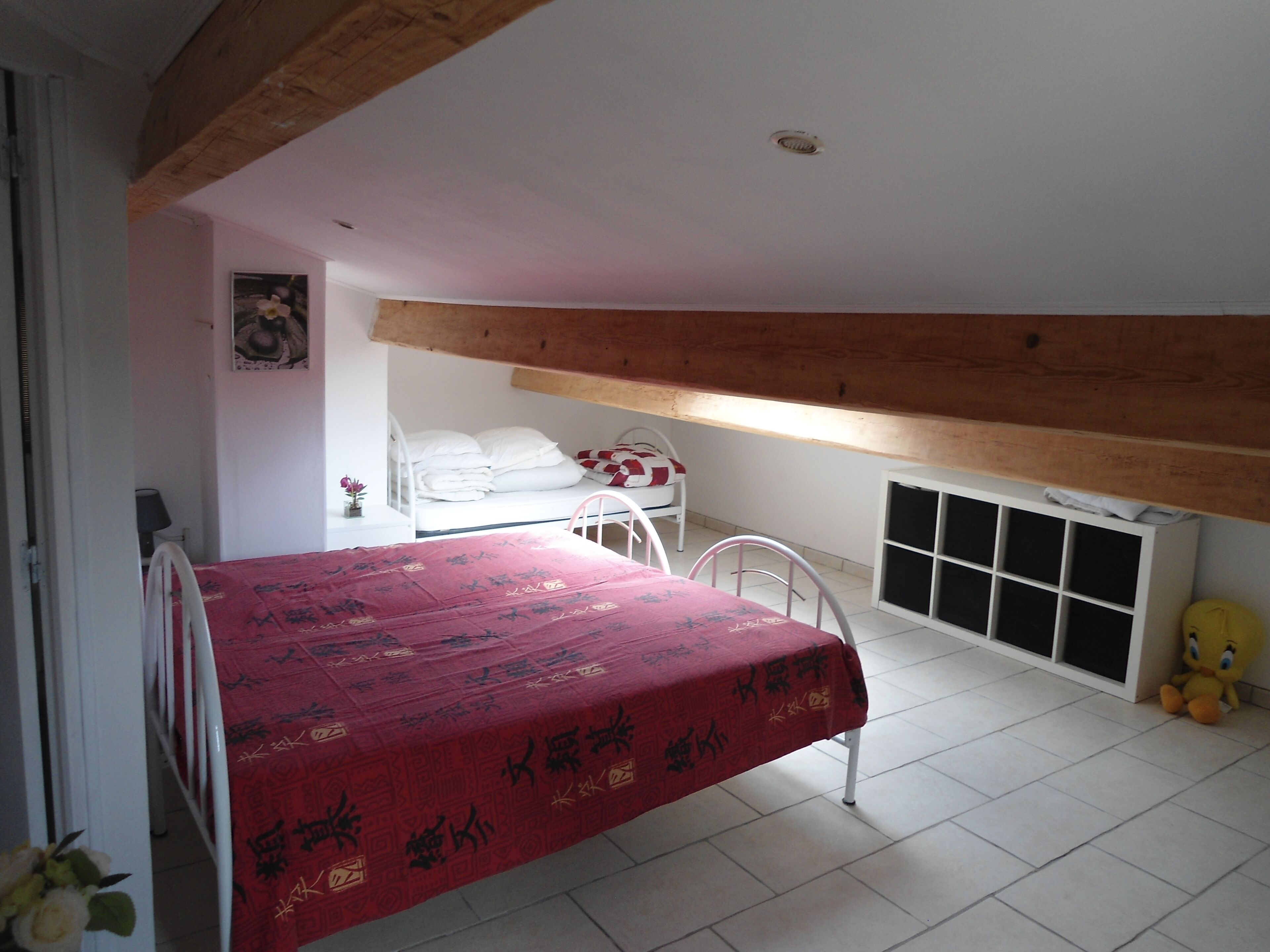A bedroom with a bed, a small table, a chair, a radiator, and a stuffed toy.