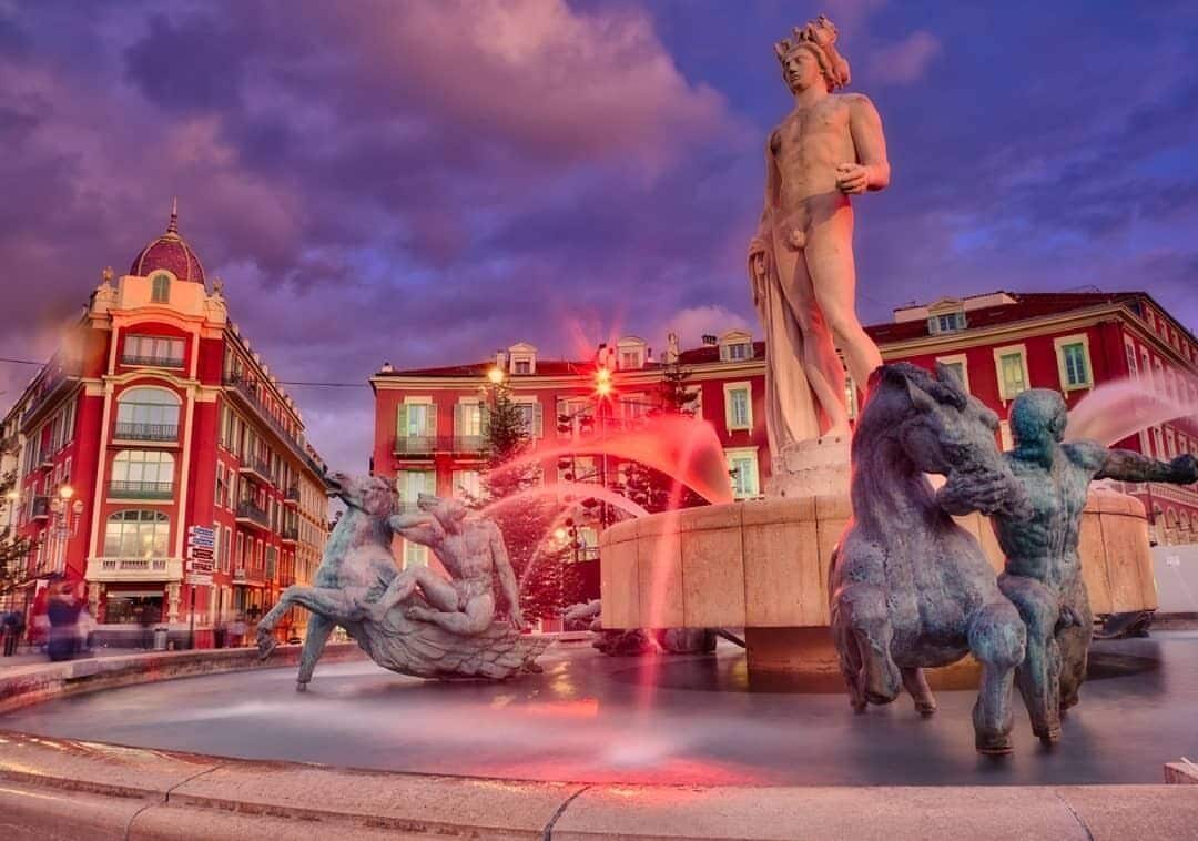 A fountain with statues, surrounded by buildings.