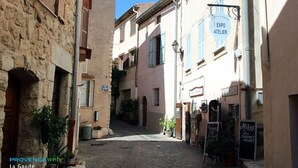 Eine schmale Gasse in La Gaude mit Kopfsteinpflaster, Steinhäusern und einem Schild für "EXPO ATELIER".