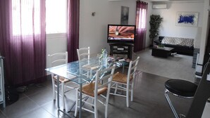 Ein modernes Wohnzimmer mit einem Glastisch, weißen Stühlen, einem schwarzen Sofa und einem Flachbildfernseher.