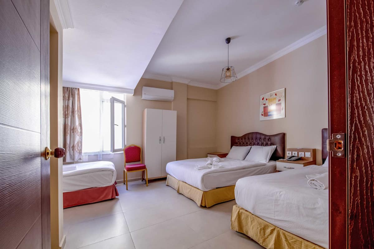 Quarto de hotel com duas camas, um guarda-roupa, uma cadeira e uma janela com cortinas.
