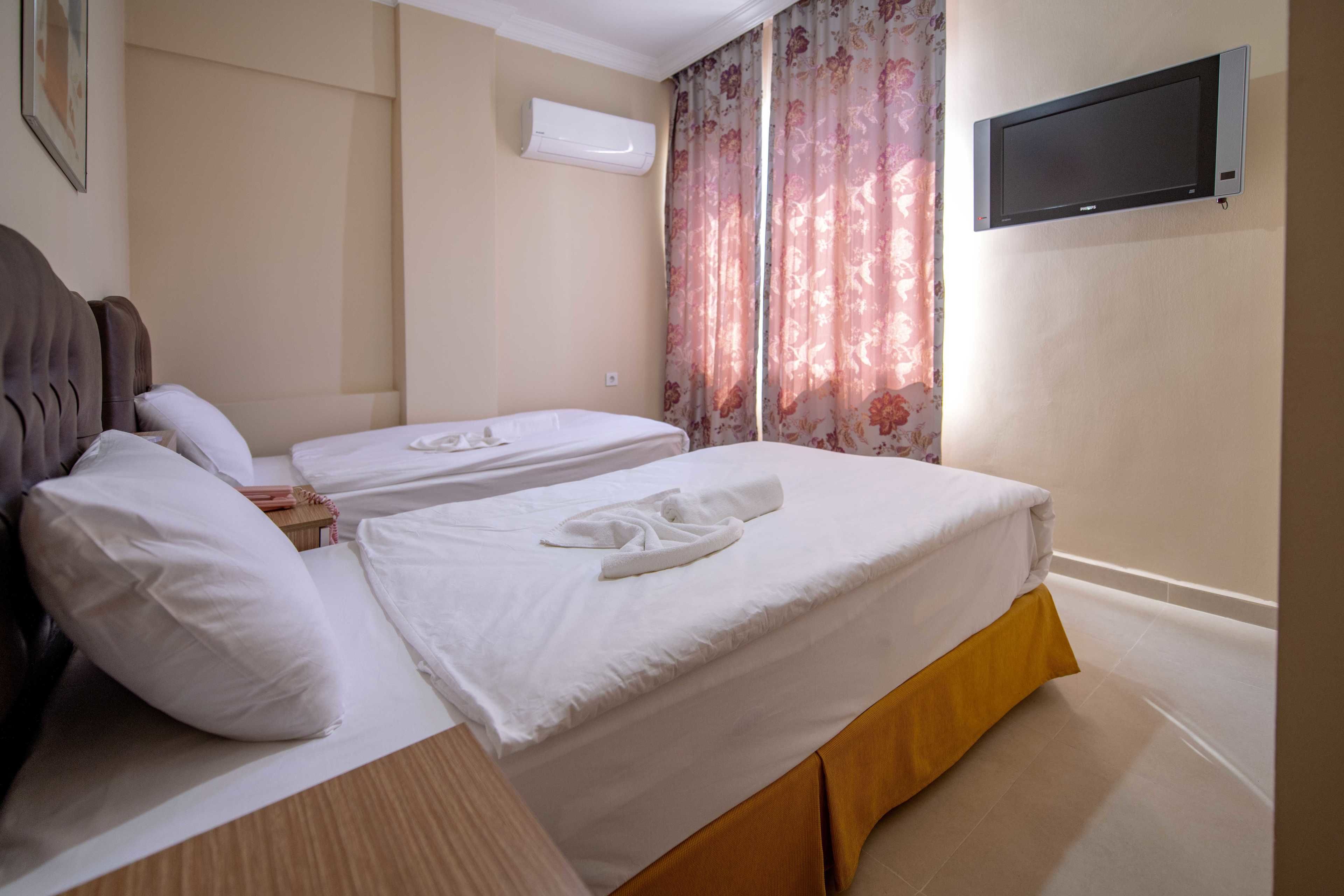 Une chambre d’hôtel avec deux lits, un téléviseur à écran plat fixé au mur et une fenêtre agrémentée de rideaux à motifs floraux.