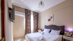 Une chambre d’hôtel avec un grand lit, un téléviseur à écran plat fixé au mur, une table de chevet avec une lampe et un tableau accroché au mur.