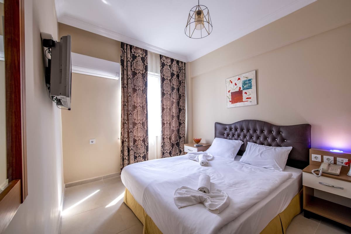 Quarto de hotel com uma cama grande, televisão de tela plana na parede, mesa de cabeceira com abajur e um quadro na parede.
