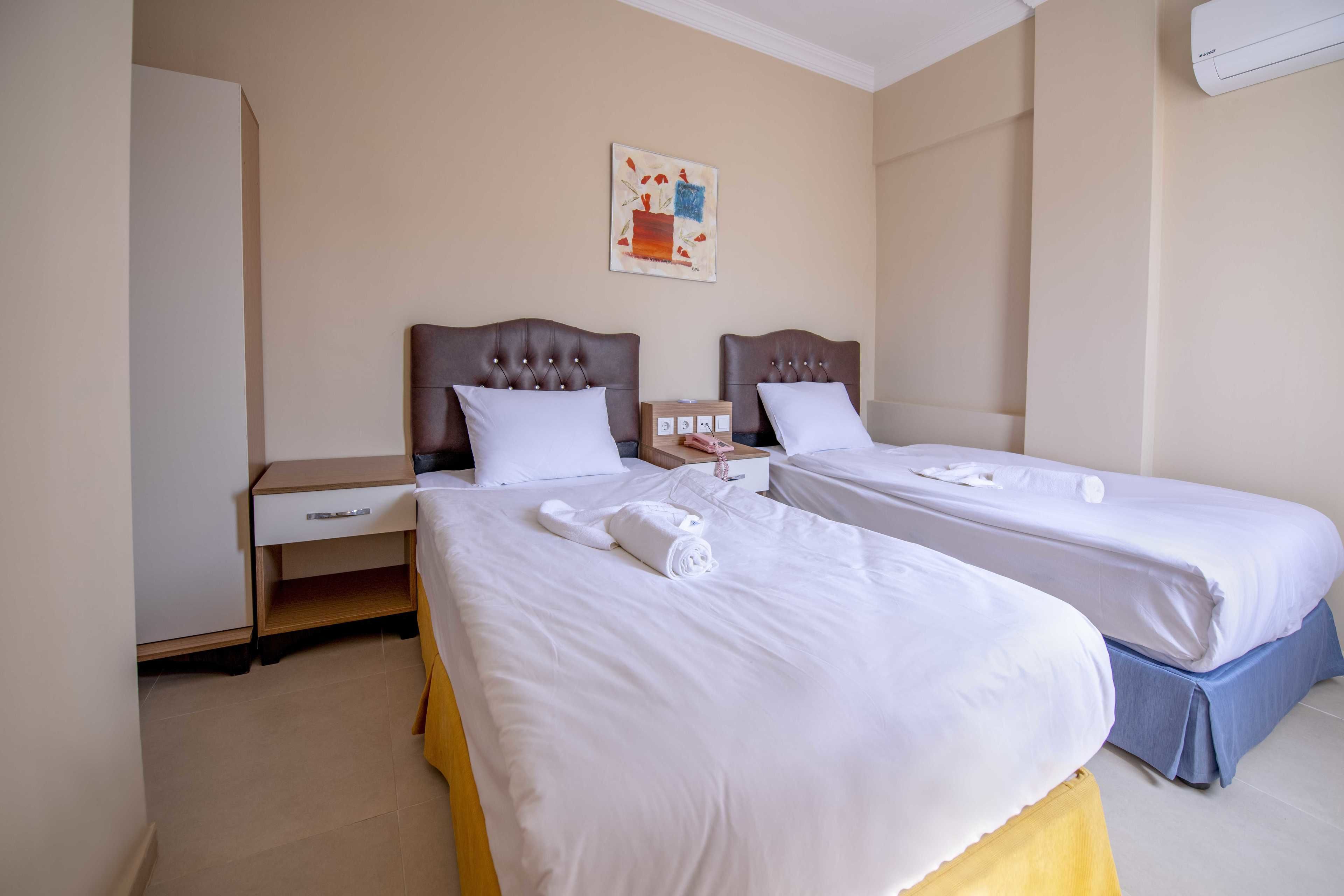 Een hotelkamer met twee bedden, een nachtkastje, een ladeblok en een schilderij aan de muur.