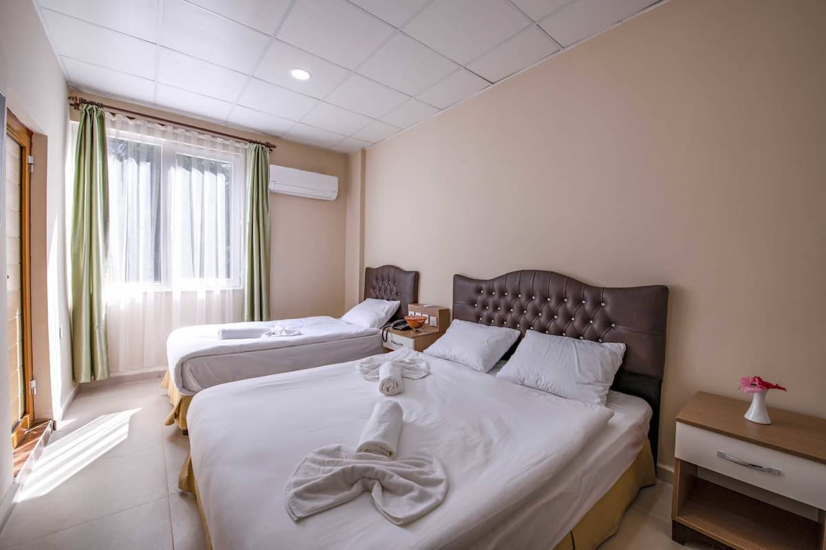 Quarto de hotel com duas camas, uma mesa de cabeceira e uma janela com cortinas.