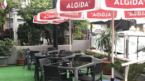 Un espace extérieur aménagé avec des tables et des chaises, entouré de plantes en pot et de parasols arborant le logo ALGIDA.