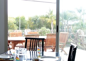Varanda com cadeiras e mesa de madeira, com vista para um jardim com árvores e cerca.