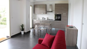 A modern kitchen with a dining area, a red sofa, and a potted plant.