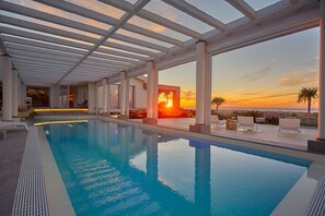 An indoor swimming pool with clear views of a sunset over the ocean, surrounded by lounge chairs and a modern architectural design. - Marsala Villa with heated pool - 5 bedrooms (marsala)