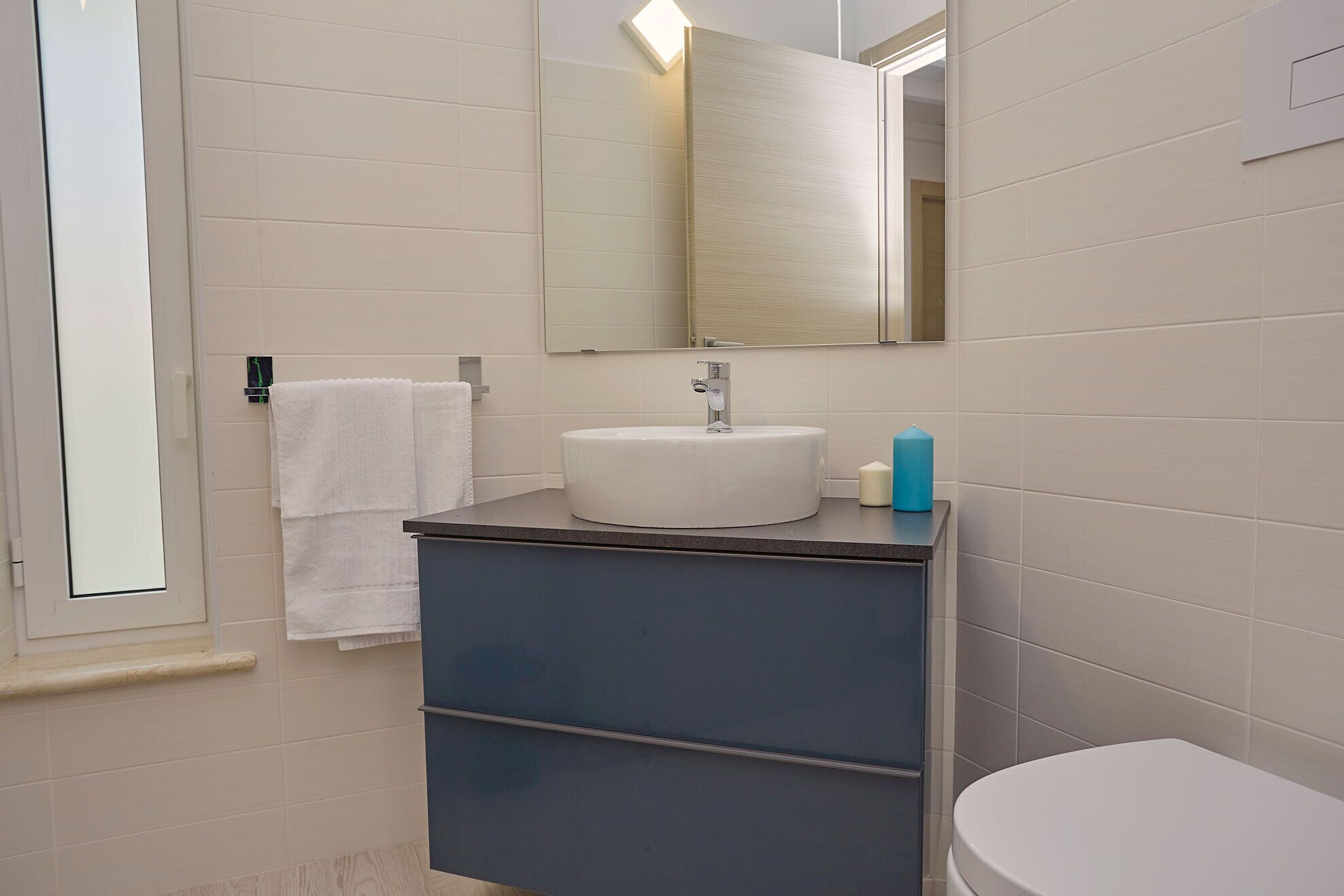 A bathroom with a white sink, a mirror above it, a blue cabinet, and a white toilet.