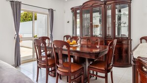 A dining area with a large wooden table, six chairs, and a glass-fronted wooden cabinet.