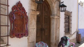 A cobblestone street with two purple chairs outside a building with a wooden door and ornate wall decorations.