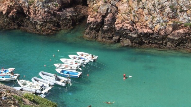 A coastal scene with boats docked at a pier, surrounded by rocky cliffs and clear turquoise water.