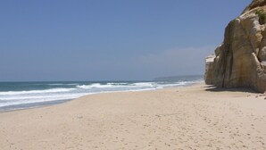 A beach with a clear sky, a sandy shore, and a rocky cliff.