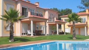 A two-story house with a swimming pool, palm trees, and a balcony with outdoor furniture.