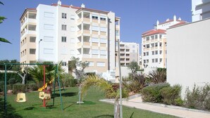 A residential area with a grassy lawn, a swing set, and a small palm tree. - Luxury quiet apartment with private pool near the beach and mountains in Algarve (Portimao)