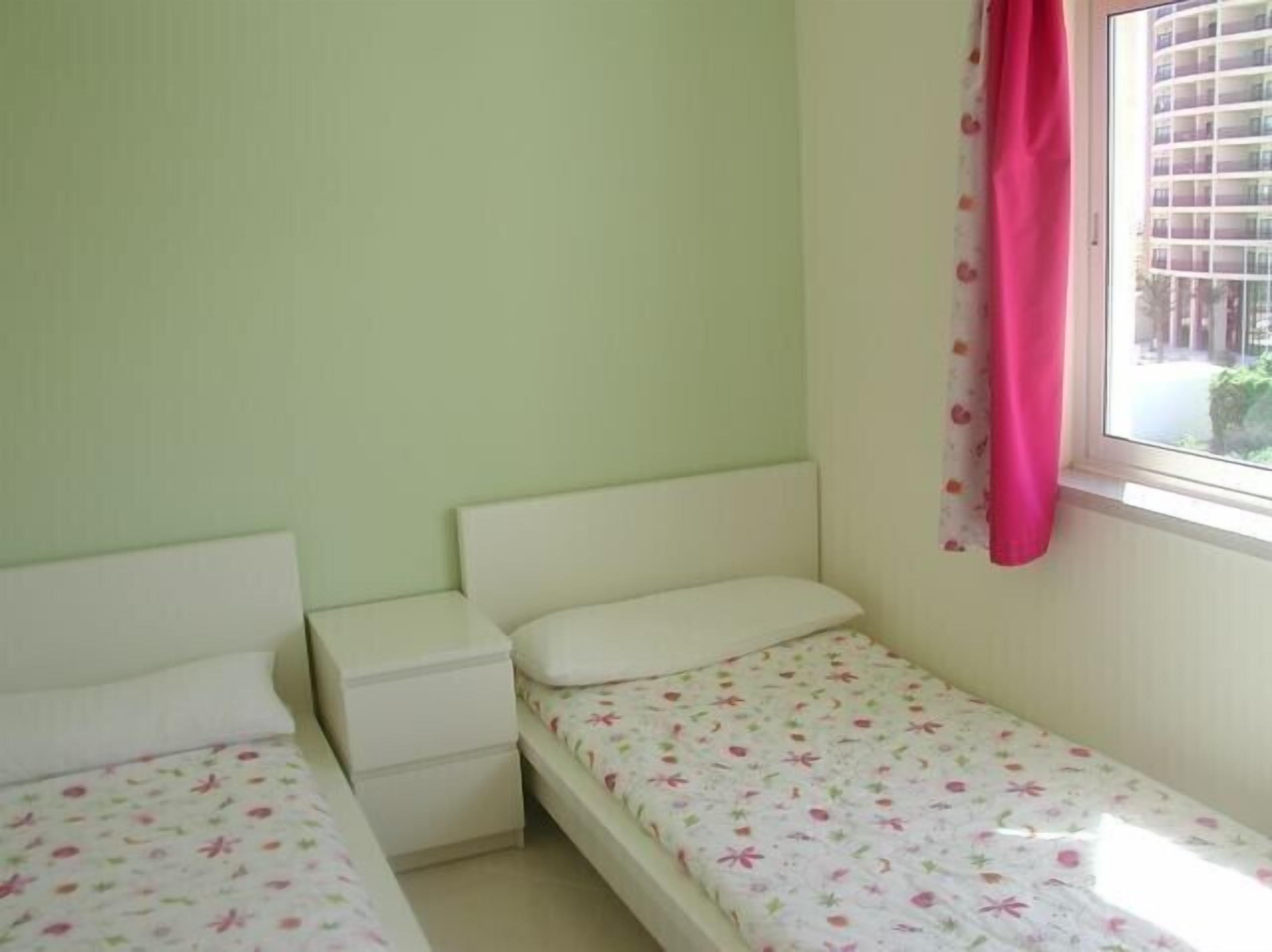 Ein kleines Einzelzimmer mit Fenster, Nachttisch und Bett mit Blumenmuster.