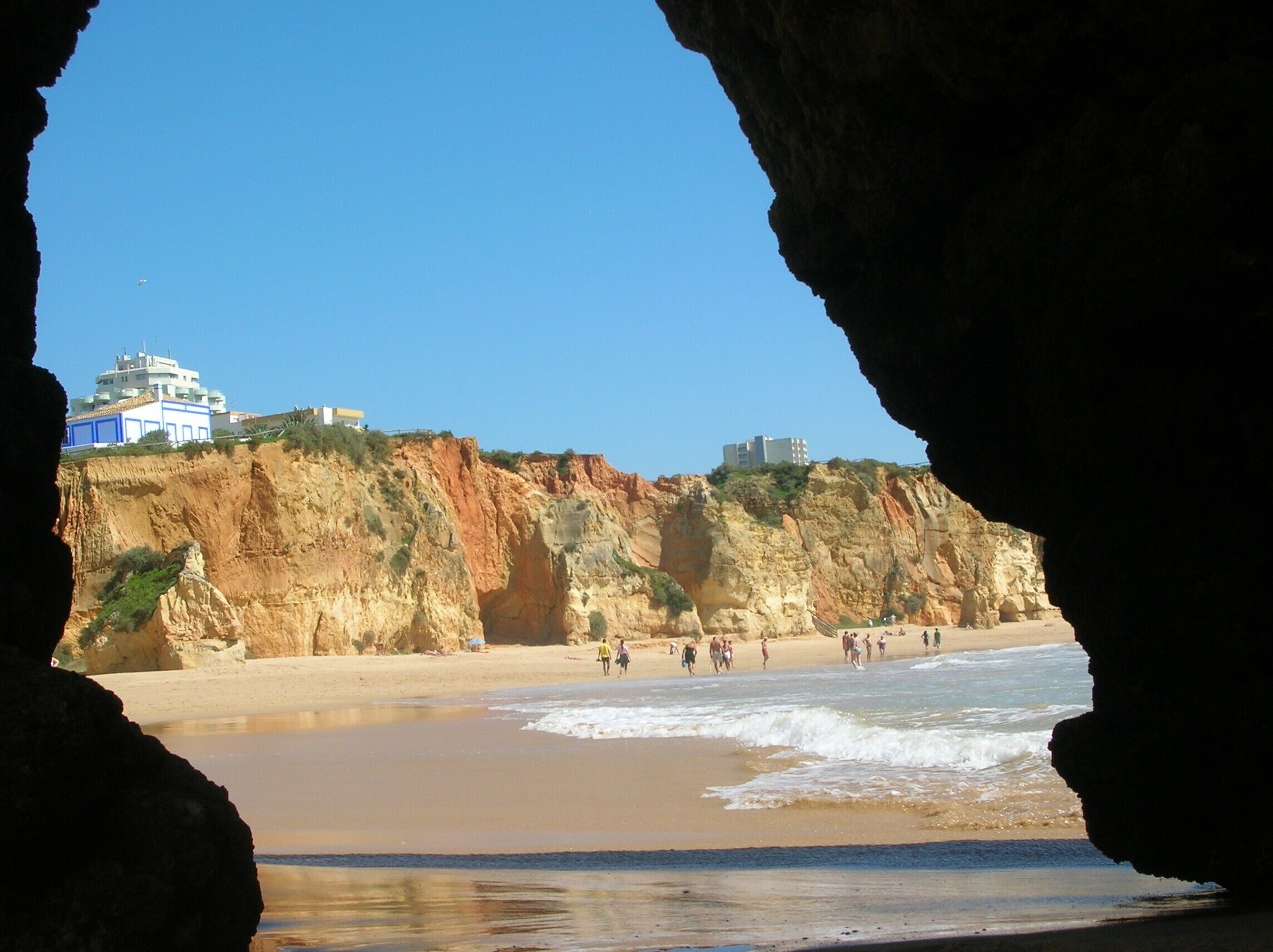 A coastal beach with cliffs and buildings in the background.