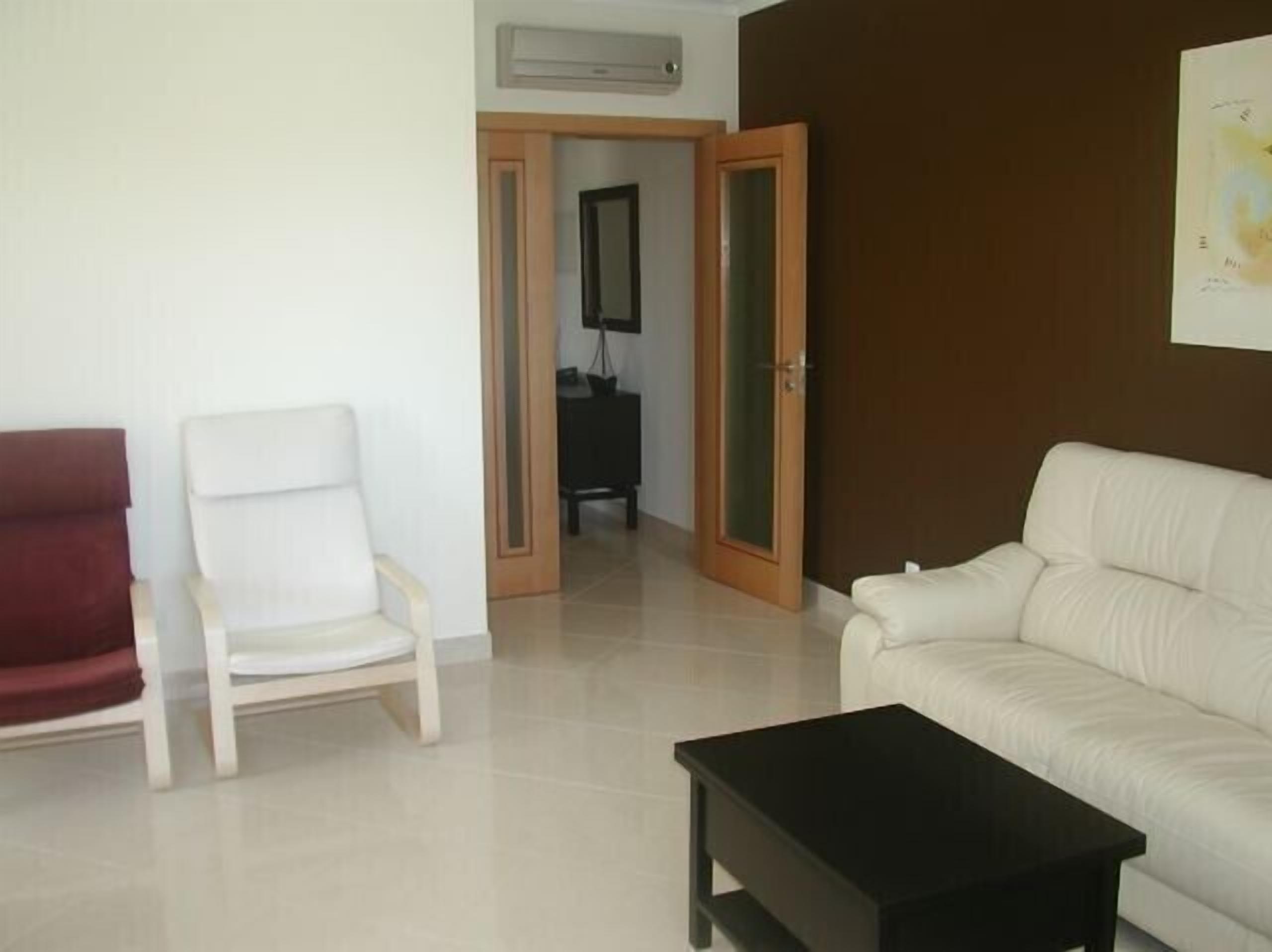 A living room with a white sofa, a red armchair, a black coffee table, and a wooden door leading to another room.