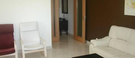 A living room with a white sofa, a red armchair, a black coffee table, and a wooden door leading to another room.