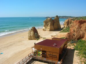 Ein Strand mit großen Felsformationen und ein hölzernes Gebäude mit rotem Dach.