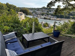 Une terrasse dotée de mobilier d’extérieur, offrant une vue sur une rivière et la ville.
