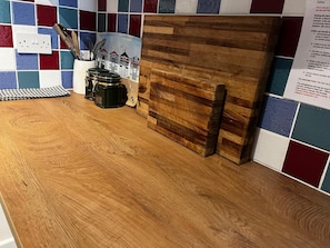 Una encimera de cocina con una tabla de cortar de madera, un bloque de cuchillos y una cafetera.