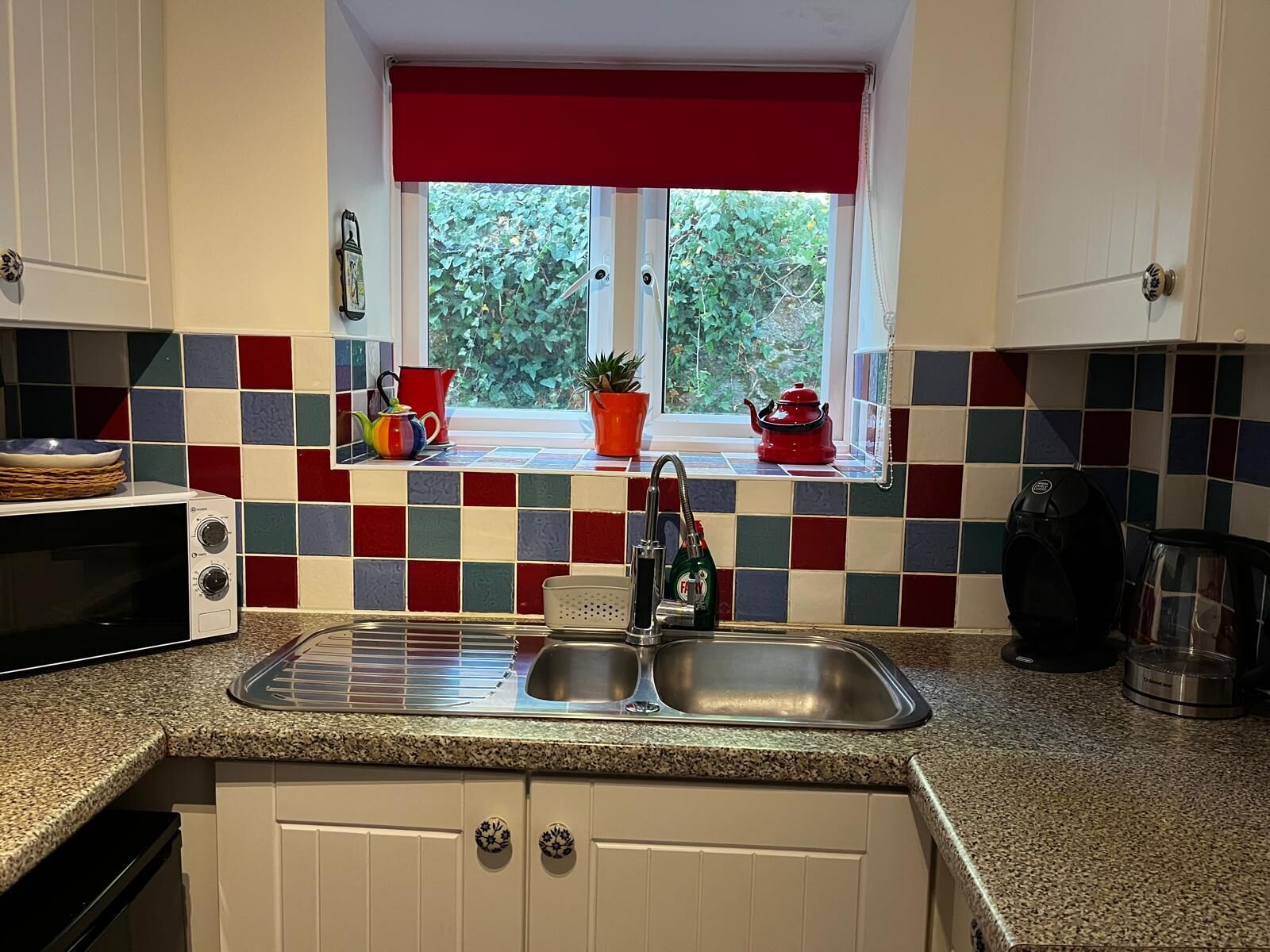 A kitchen with a window, a sink, a microwave, and a kettle.
