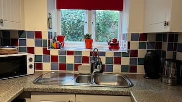 A kitchen with a window, a sink, a microwave, and a kettle.