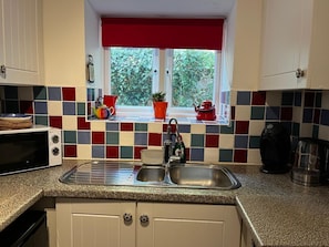 Una cocina con ventana, un lavamanos, un microondas y una tetera.