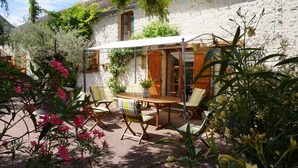 A rustic outdoor seating area with a wooden table and chairs, surrounded by lush greenery and flowering plants. - Country Cottage / Gite - Poligny (Poligny)