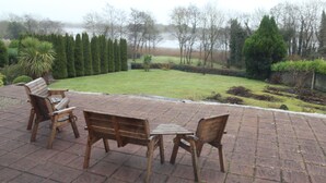 A patio with wooden furniture and a view of a landscaped garden and trees. - Family Retreat With Panoramic Lake View And Large Front And Back Gardens (Newmarket-On-Fergus)