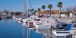 Un puerto deportivo con varias embarcaciones amarradas, una superficie acuática tranquila y una hilera de edificios al fondo.