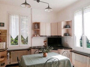 A compact kitchen with a dining table, built-in cabinets, a radiator, and a window with curtains. - House with garden (Port-Saint-Louis-Du-Rhône)