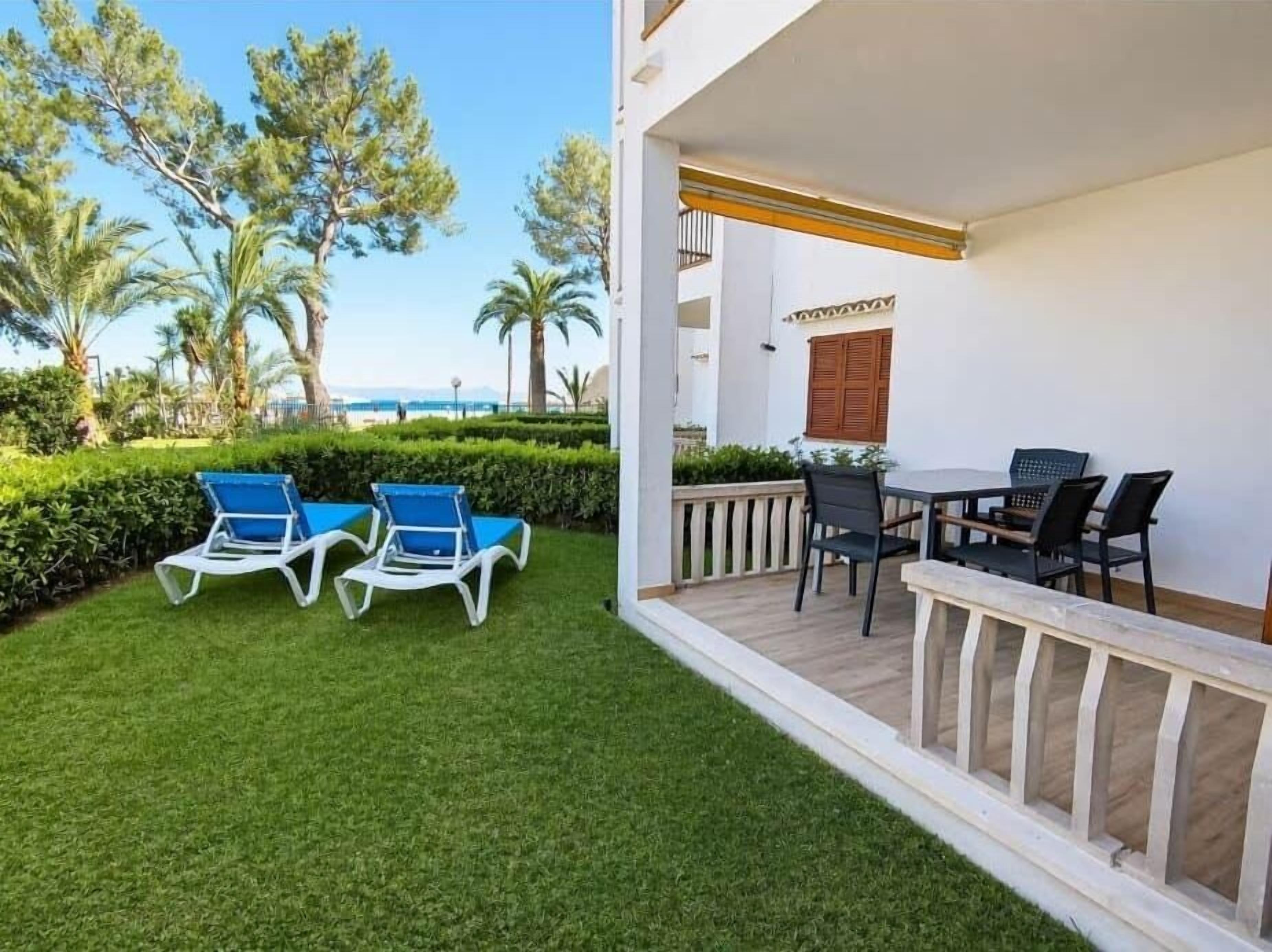 A balcony with a table and chairs, a view of the sea, and a well-maintained lawn.