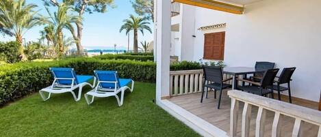 A balcony with a table and chairs, a view of the sea, and a well-maintained lawn.