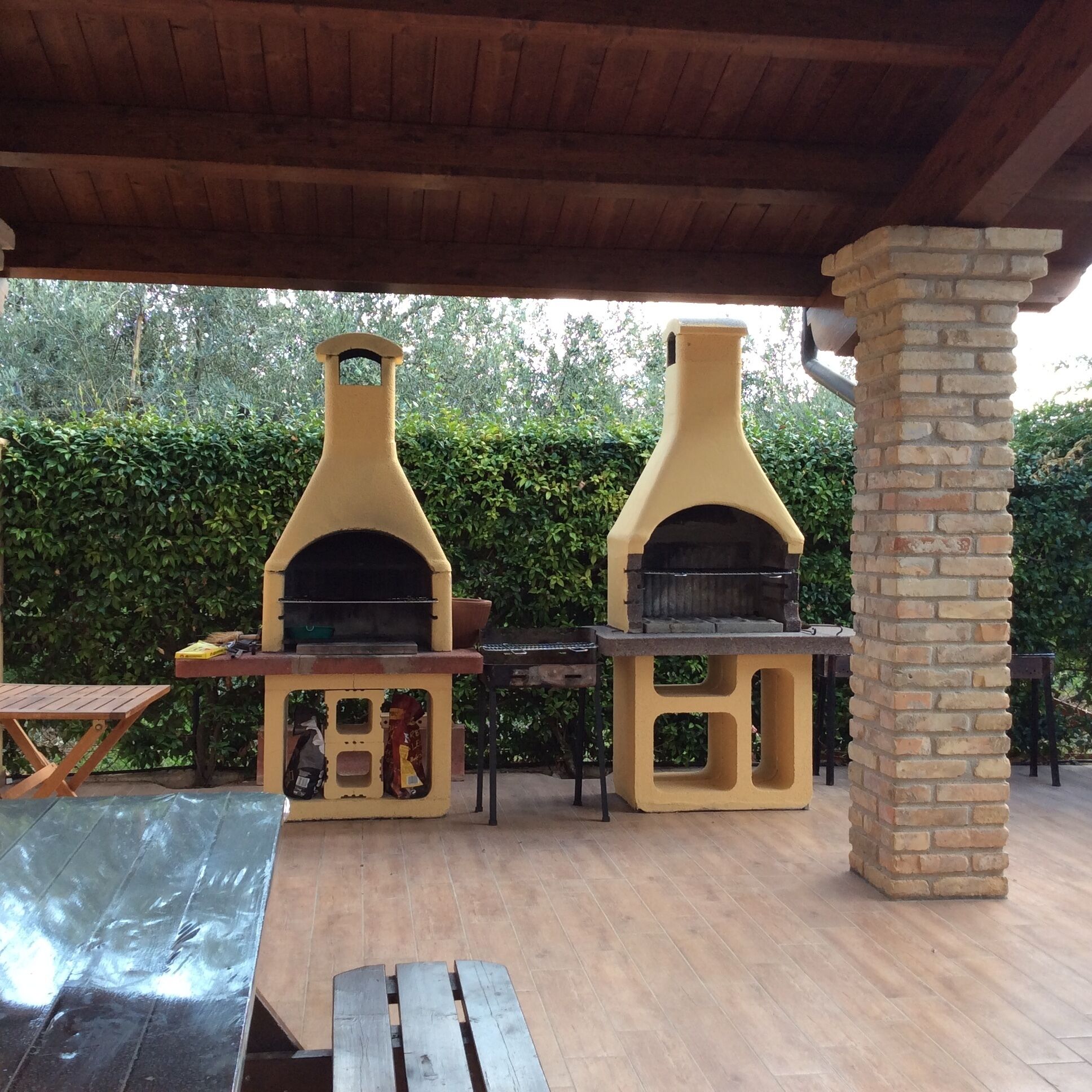 Une terrasse extérieure avec deux fours à pizza en briques, une table en bois et un pilier en briques.