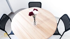 A round wooden table with a clear glass vase containing flowers, surrounded by black chairs.
