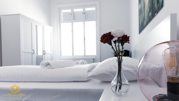 A hotel room with a neatly made bed, a vase with flowers, and a lamp on a bedside table.