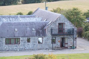 A stone building with a sloped roof, a balcony, and a gravel driveway.