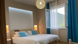 Une chambre à coucher avec un lit, des lampes de chevet, une fenêtre avec des rideaux et une vue sur la verdure à l’extérieur.