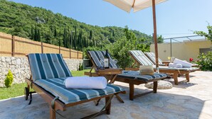 Une terrasse dotée de chaises longues et d’un parasol, offrant une vue sur une colline verdoyante.