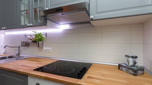 Une cuisine moderne avec des meubles gris, une hotte en acier inoxydable, un plan de travail en bois, une cuisinière encastrée et une petite plante en pot.