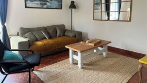Een woonkamer met een bank, een salontafel, een stoel, een vloerlamp, een spiegel en een schilderij aan de muur.