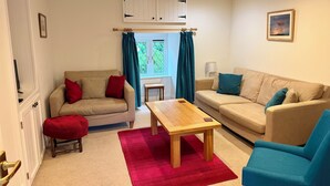 Un salon avec deux canapés beige, une table basse en bois, un tapis rouge et un fauteuil bleu.